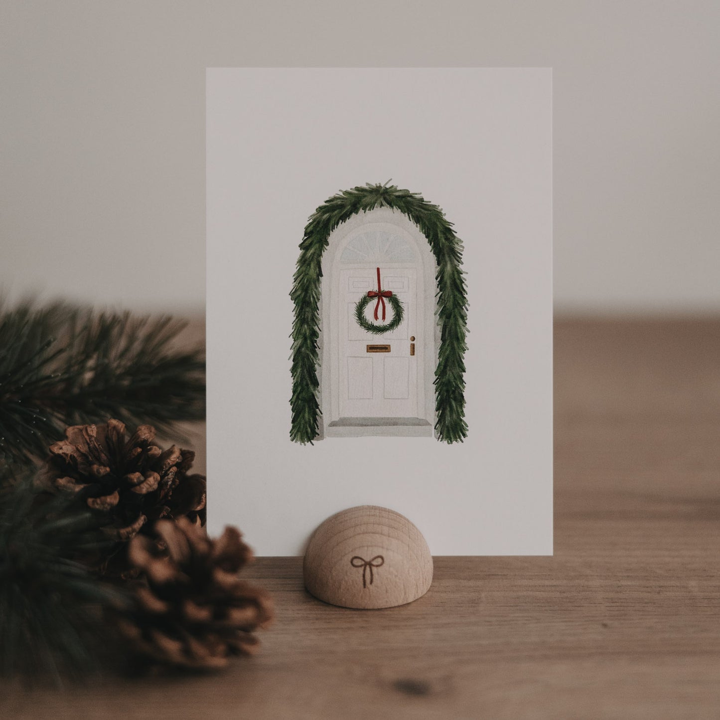 Weihnachtskarte mit weißer Tür, geschmückt mit grünem Türkranz und Tannengirlande