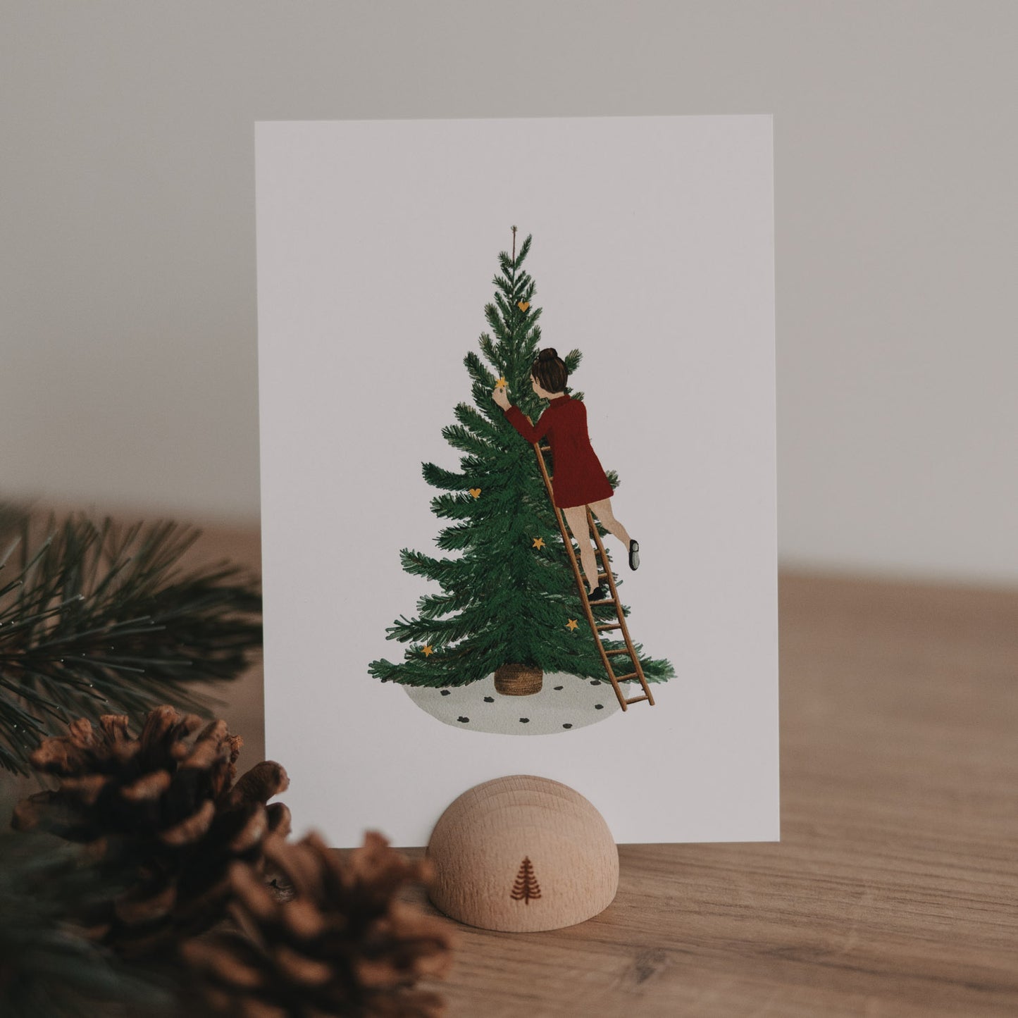 Weihnachtskarte mit Illustration einer Frau, die einen Tannenbaum mit Sternen dekoriert