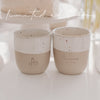 Zwei Limited Edition Keramikbecher in Beige und Weiß mit geprägten Motiven stehen nebeneinander auf einem Tisch.