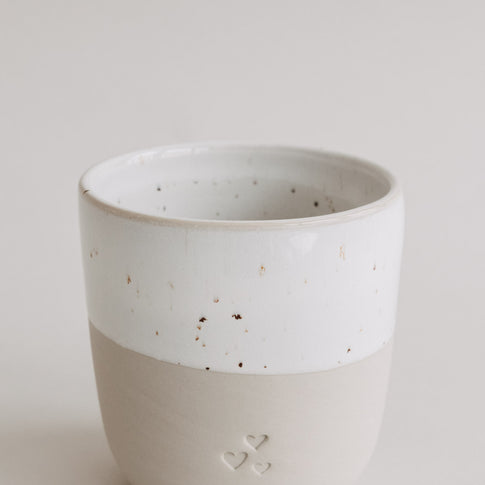 Nahaufnahme des Keramikbechers in Beige und Weiß mit feinen Sprenkeln und Herzdetails.