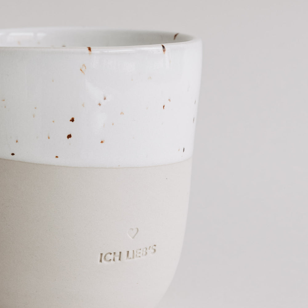 Nahaufnahme der „Ich lieb’s“-Tasse mit heller Glasur und Sprenkeln, Fokus auf Prägung.