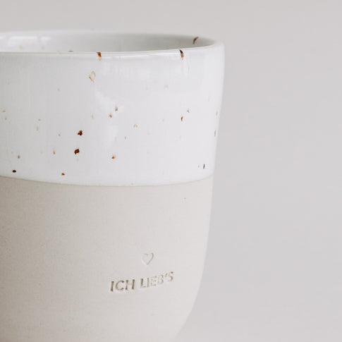 Nahaufnahme der „Ich lieb’s“-Tasse mit heller Glasur und Sprenkeln, Fokus auf Prägung.