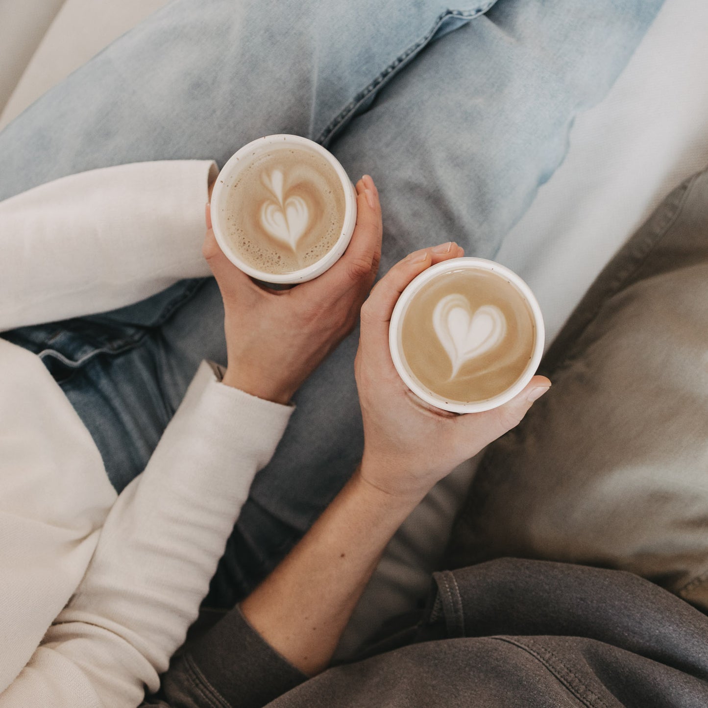 Zwei Hände halten Becher mit Latte-Art-Herzen, harmonische MR/MRS-Motivszene aus der Vogelperspektive.
