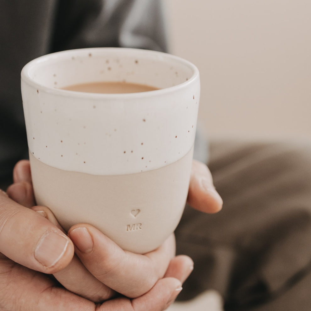 Nahaufnahme einer Person, die den MR-Becher seitlich hält, sichtbare Sprenkelglasur und MR-Prägung.
