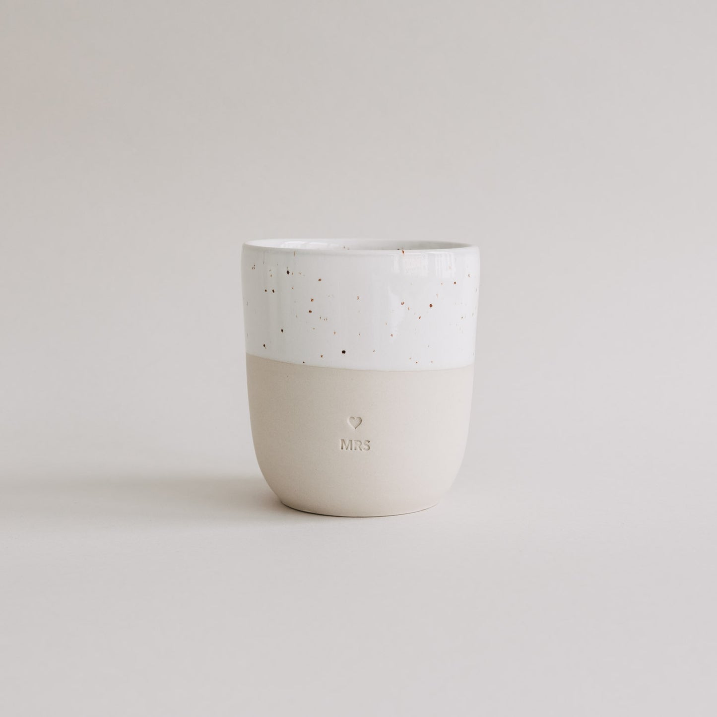Keramikbecher MRS in Beige und Weiß mit Herzprägung auf hellem Hintergrund.