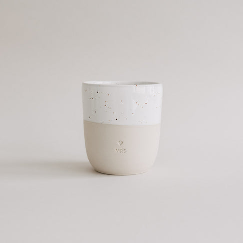 Keramikbecher MRS in Beige und Weiß mit Herzprägung auf hellem Hintergrund.