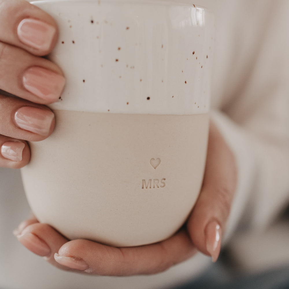 Nahaufnahme: Hände halten MRS Becher mit weißer gesprenkelter Glasur.