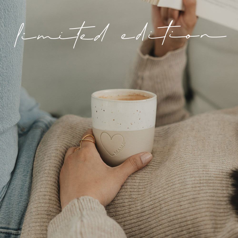Keramikbecher Mama mit Herzdetail, gefüllt mit Kaffee, gemütlich auf Sofa