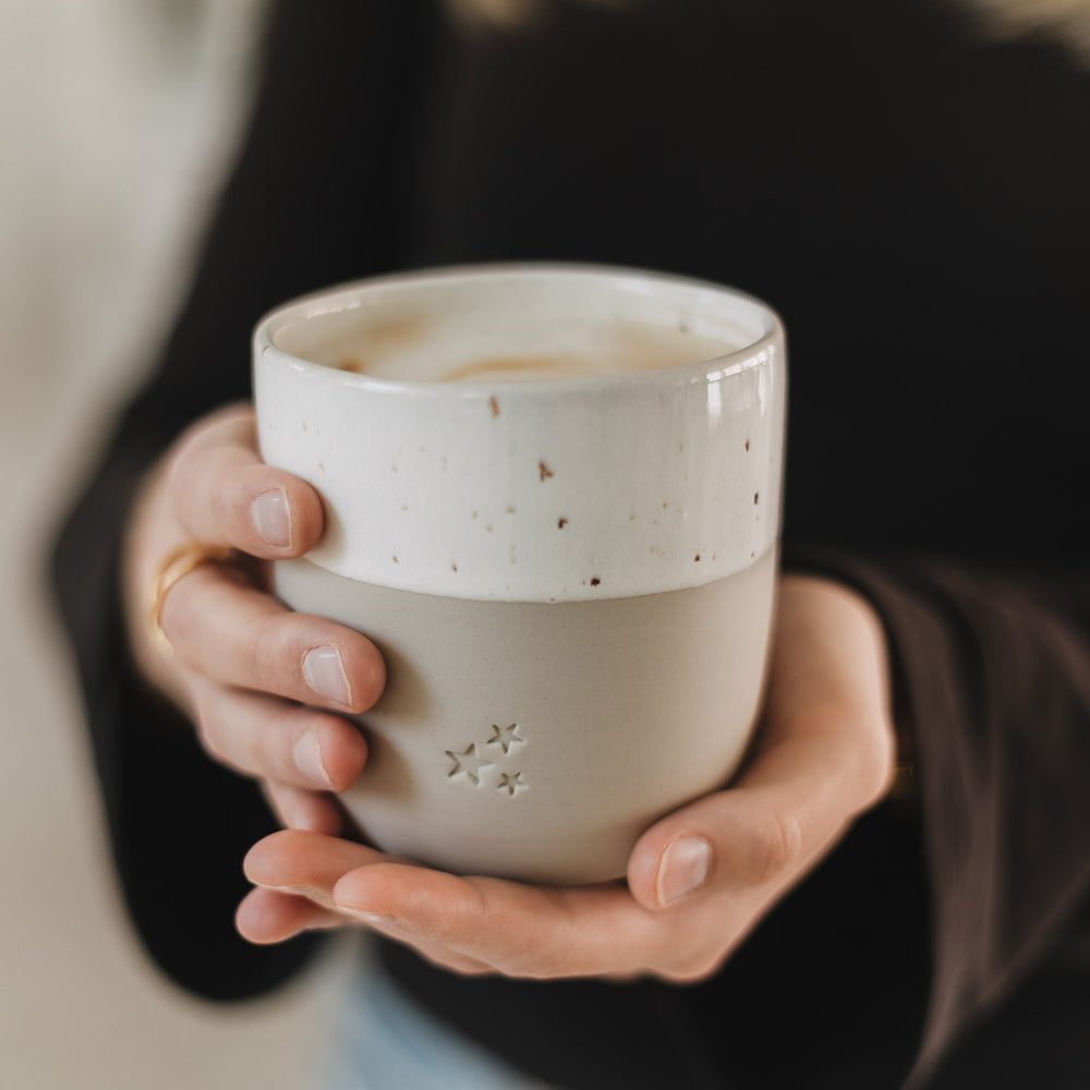 Keramikbecher mit Sternprägung in der Hand, gefüllt mit Kaffee, minimalistisches Design
