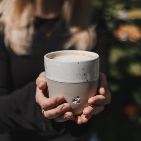 Keramikbecher mit Sternmotiv in beiden Händen, gemütliche Atmosphäre mit Heißgetränk