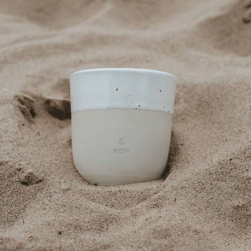 Steingutbecher Moin im Sand fotografiert mit nordischer Strandstimmung