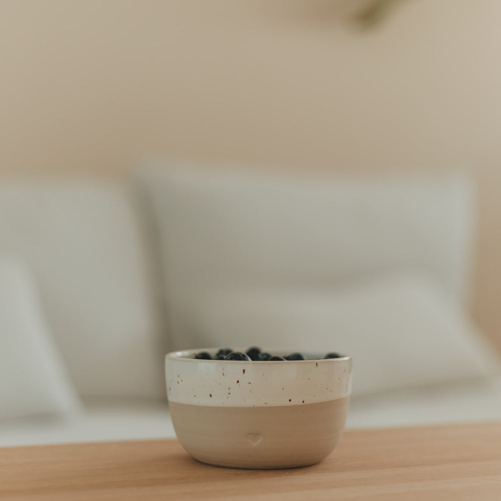 Keramikschale mit Herz in Beige und Weiß, gefüllt mit Heidelbeeren auf einem Holztisch