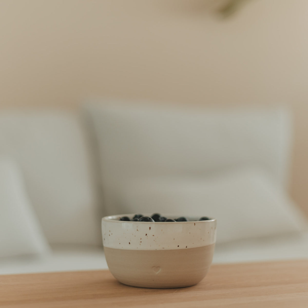Keramikschale mit Herz in Beige und Weiß, gefüllt mit Heidelbeeren auf einem Holztisch