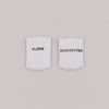 Zwei weiße Babysocken mit schwarzem Schriftzug „Kleine Schwester“ auf hellem Hintergrund.