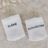 Babysocken „Kleine Schwester“ auf strukturierter  Unterlage und Blättern.