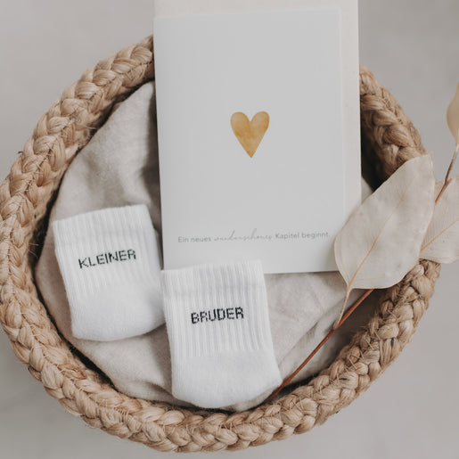 Babysocken „Kleiner Bruder“ im Korb mit Geburtskarte und Herzsymbol