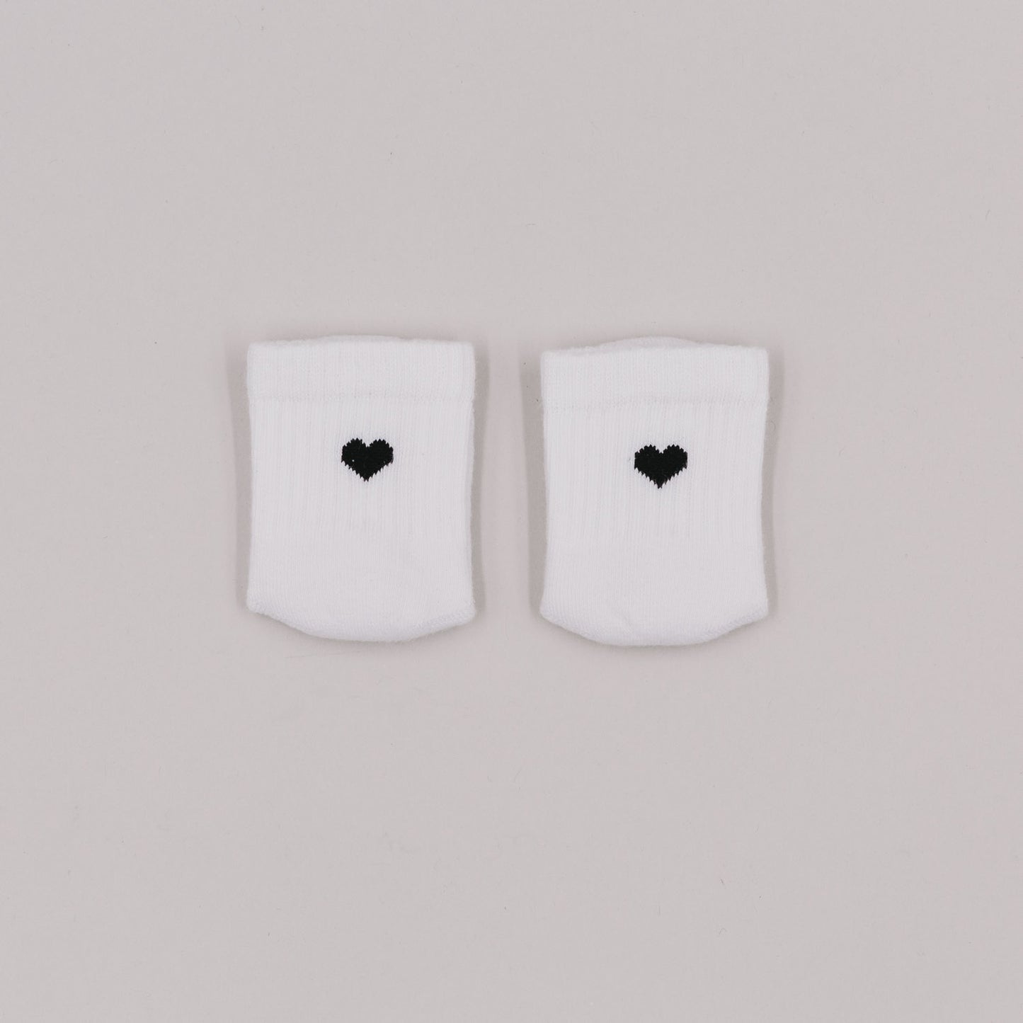 Weiße Babysocken mit gesticktem schwarzen Herz auf hellem Hintergrund, liebevoll nebeneinander drapiert.