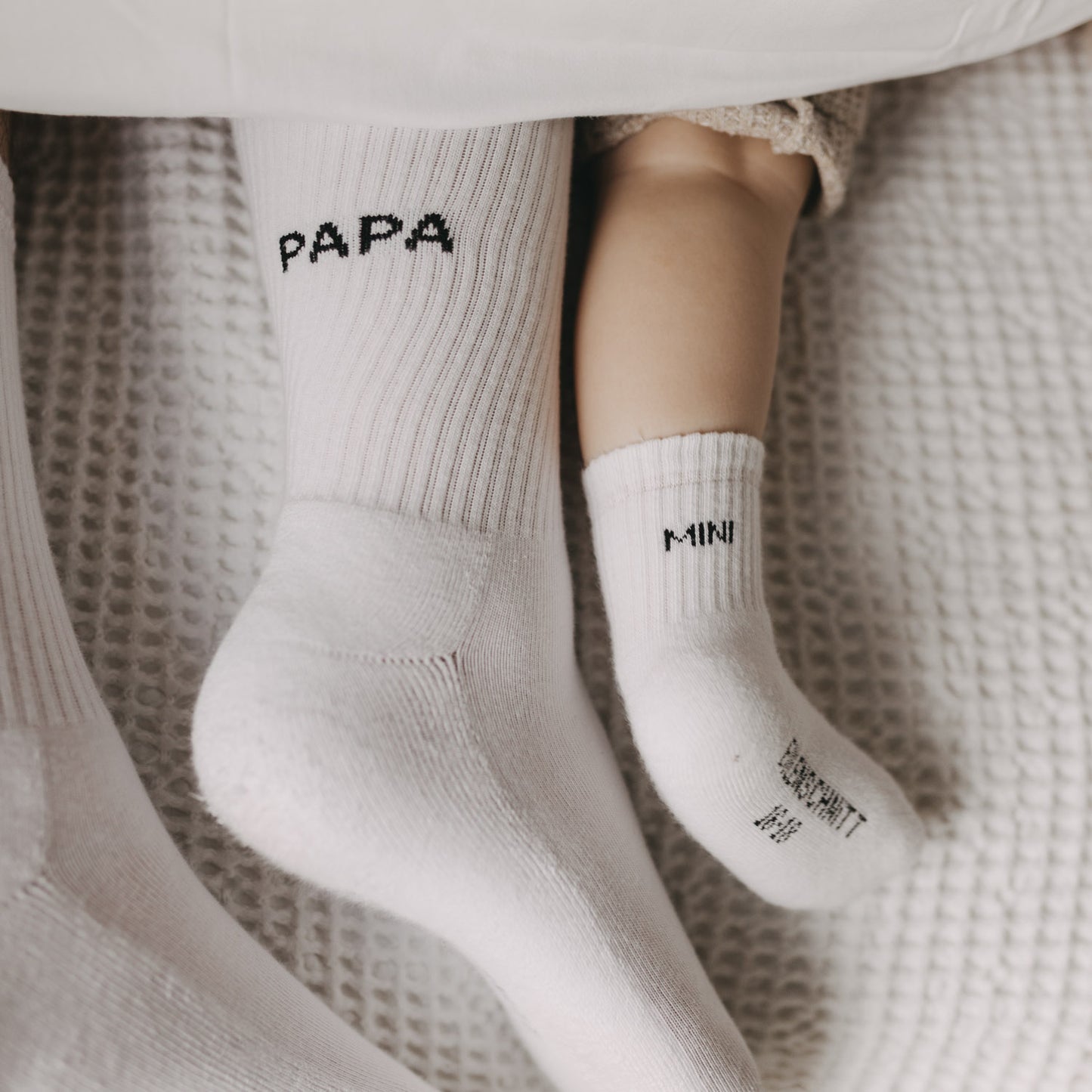 Kuschelige Familienmomente mit Papa- und Mini-Socken auf weichem Bett.
