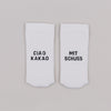 Weiße Socken mit schwarzer Stickerei „Ciao Kakao“ und „Mit Schuss“ auf neutralem Untergrund nebeneinander liegend