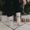 Rückansicht einer Person in den Mistletoe-Socken mit Mistelzweig in der Hand vor weihnachtlich geschmücktem Baum