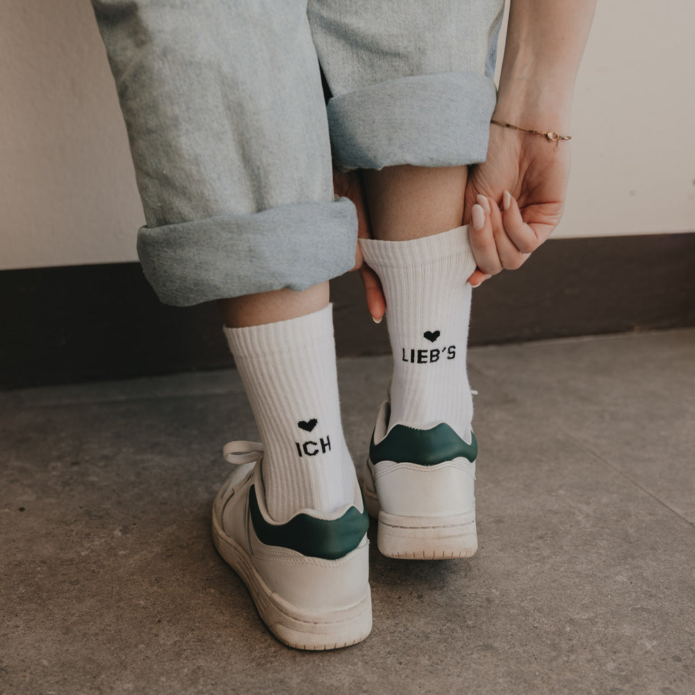 Detailaufnahme weißer Socken mit Schriftzug „Ich lieb’s“ und Herzmotiv am Knöchel