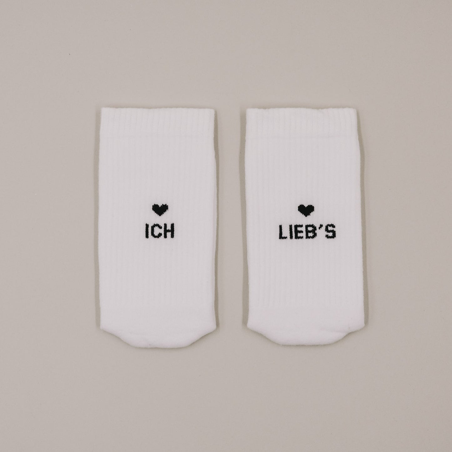 Flachliegende weiße Socken mit Aufdruck „Ich lieb’s“ und kleinem Herzmotiv
