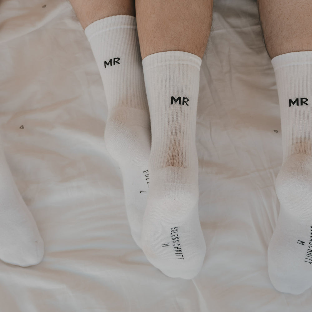 Weiße Socken „MR“ am Fuß in Nahaufnahme auf hellem Stoff