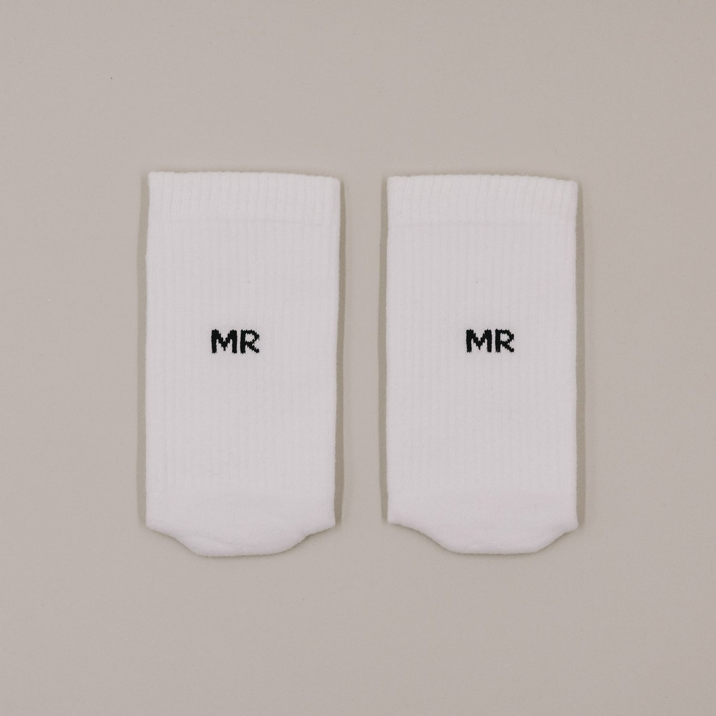 Flachliegende weiße Socken mit „MR“ Schriftzug in minimalistischer Darstellung