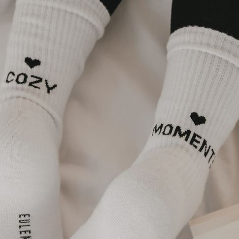 Detailaufnahme weißer Socken „Cozy Moments“ mit schwarzem Schriftzug und Herz