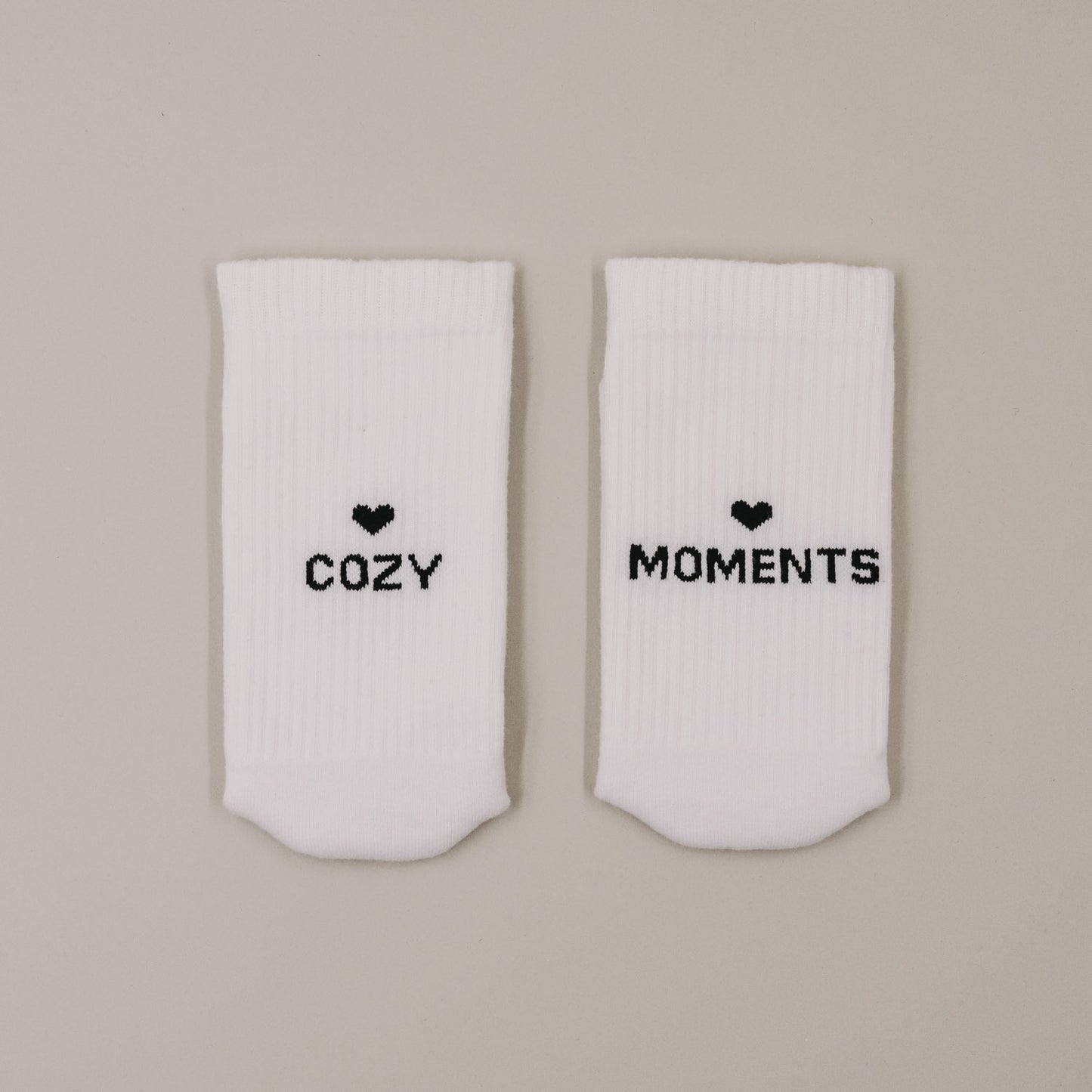 Flachliegende weiße Socken „Cozy Moments“ mit Herzsymbol und Schriftzug minimalistisch präsentiert