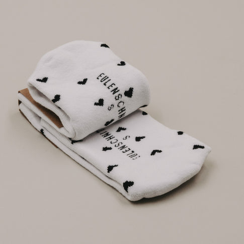 Gefaltete weiße Socken mit schwarzen Herzchen und Eulenschnitt Logo Detailansicht