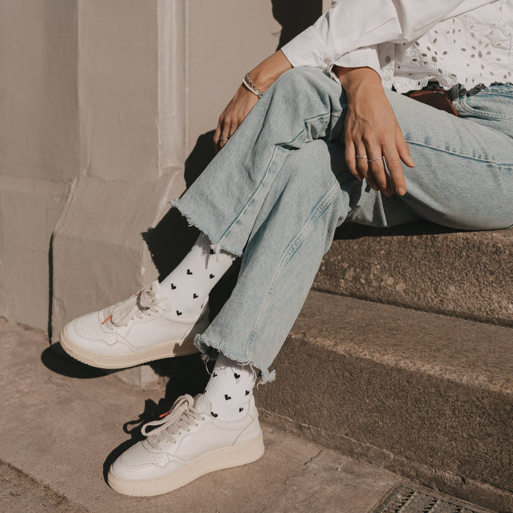Weiße Herz-Socken in lässigem Outfit beim Sitzen auf Treppe mit Jeans und Sneakern