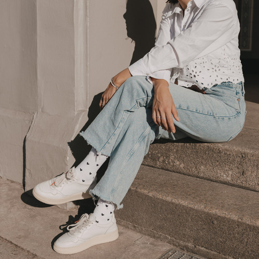 Frau mit weißen Socken mit schwarzen Herzen, kombiniert mit Jeans und weißer Bluse