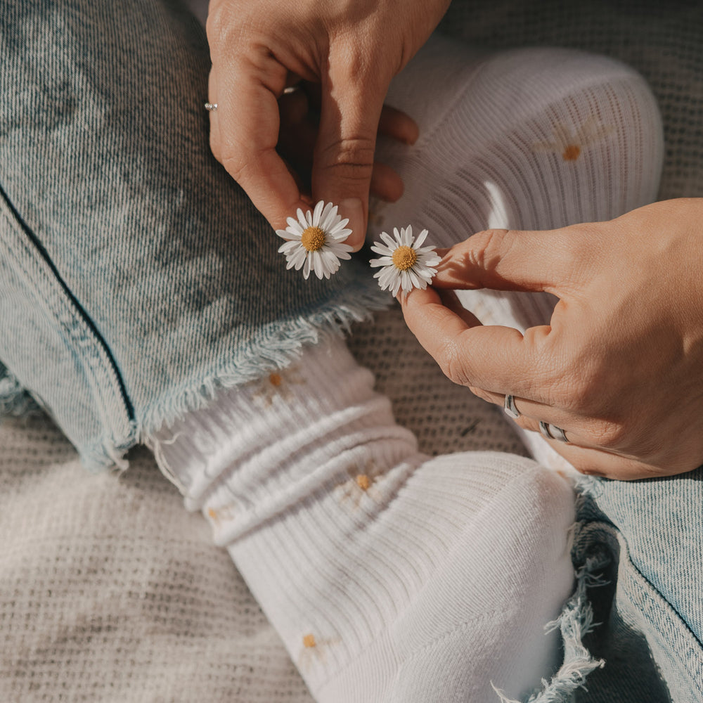 Weiße Socken mit zartem Gänseblümchen-Muster, kombiniert mit Jeans im natürlichen Licht