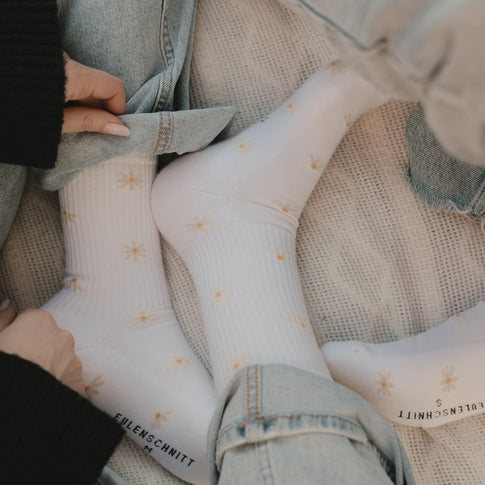 Weiße Socken mit Daisy-Muster lässig getragen zu Jeans auf gemütlicher Oberfläche