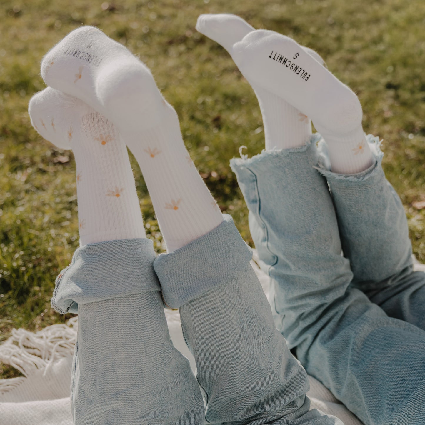 Zwei Personen tragen weiße Socken mit Gänseblümchen-Muster im natürlichen Outdoor-Look