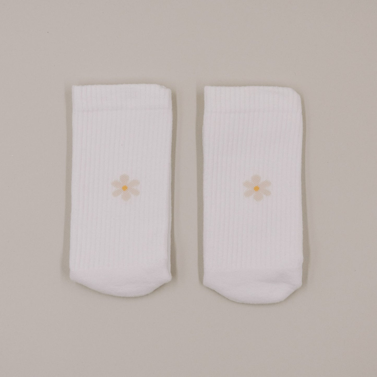 Minimalistische Produktansicht weißer Socken mit kleinem Daisy-Motiv auf hellem Hintergrund