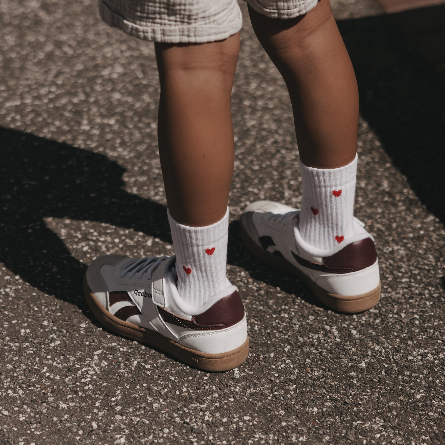 Weiße Eulenschnitt Kindersocken mit roten Herzen, getragen zu hellen Sneakern.