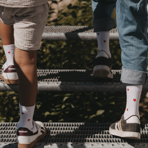 Zwei Kinder tragen Eulenschnitt Kindersocken mit roten Herzen beim gemeinsamen Treppensteigen.