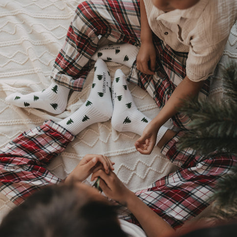 Familie trägt weiße Eulenschnitt Socken mit grünen Tannen zur Weihnachtszeit