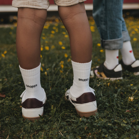 Kids Socken Großer Bruder in Weiß mit schwarzem Schriftzug zu Sneakern auf einer Wiese