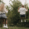 Kinder auf Schaukel im Garten, tragen weiße „Be Happy“ Socken mit Herz