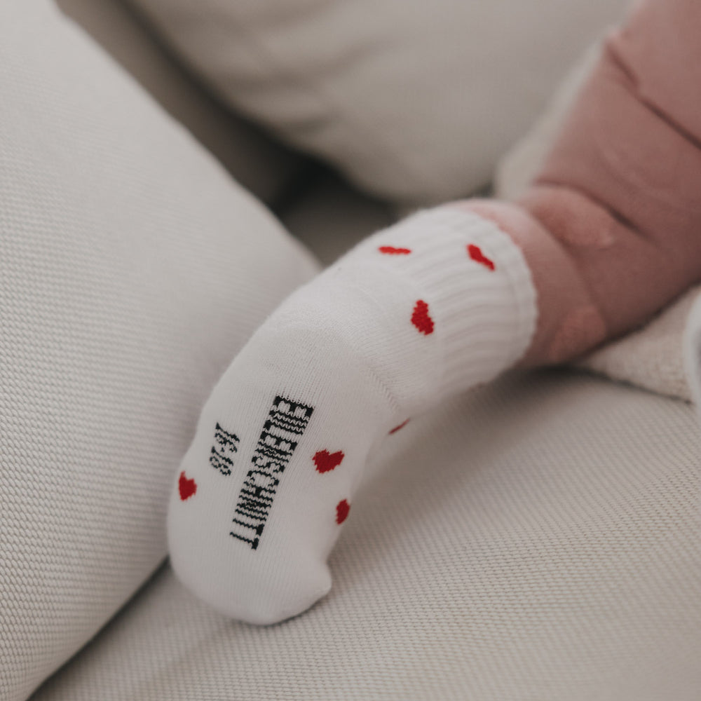Nahaufnahme Babyfuß mit weißen Socken und roten Herzen, Sohle sichtbar