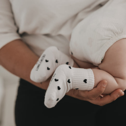 Baby liegt auf Arm mit weißen Socken und schwarzen Herzen, gemütliche Nahaufnahme