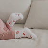 Detail Babyfuß mit weißen Socken und roten Zuckerstangen, weiches Material und gemütlicher Look