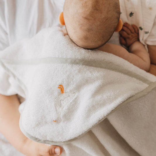 Rückansicht eines Babys, das in ein weißes Kapuzenhandtuch mit zartem Gänse-Stickmotiv eingehüllt ist. Die weiche Frottee-Qualität und die großzügige Kapuze machen das Handtuch zum idealen Begleiter nach dem Baden.