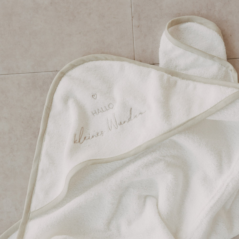 Kapuzenhandtuch Baby aus Baumwolle mit Schriftzug Hallo kleines Wunder auf hellem Hintergrund