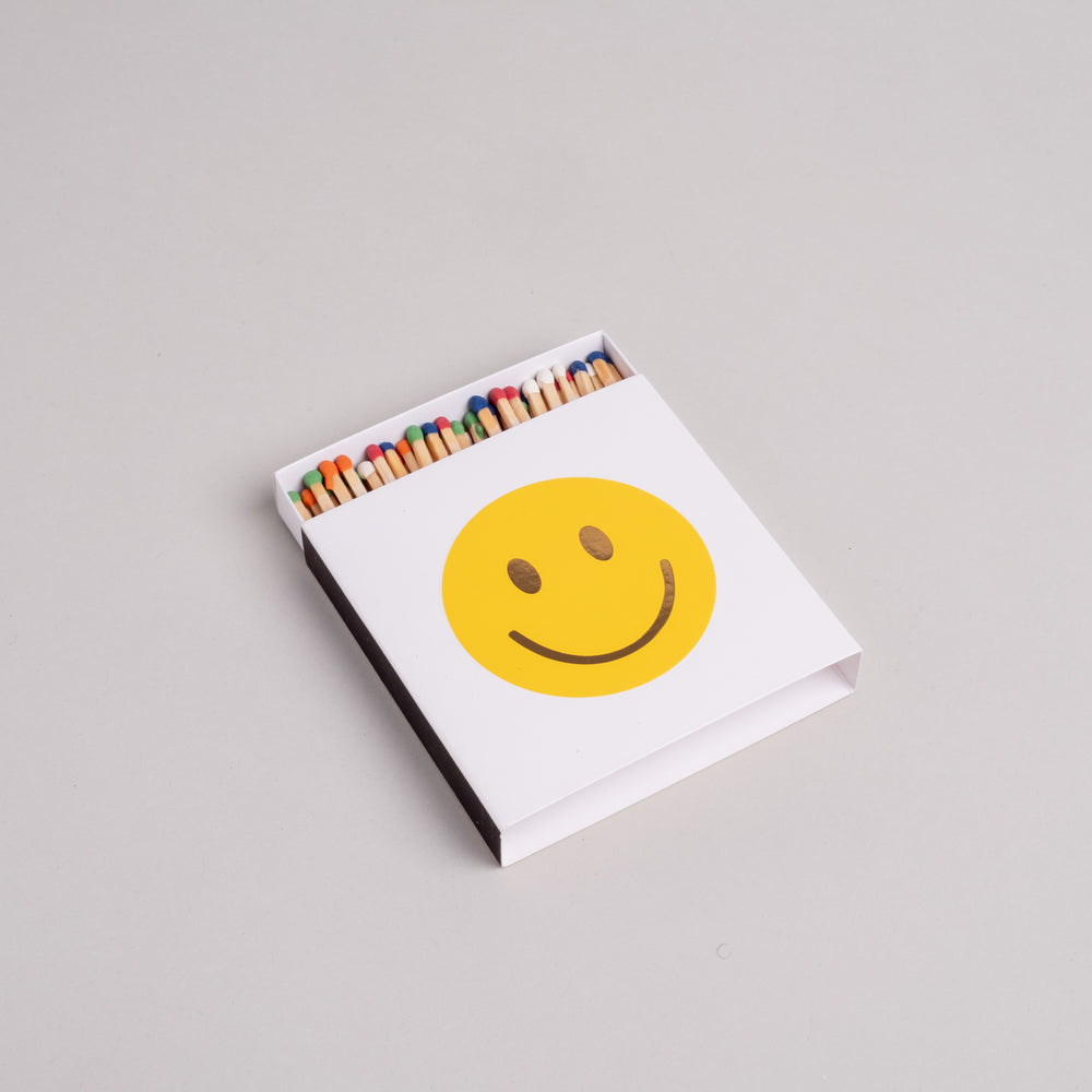 Geöffnete Streichholzschachtel mit gelbem Smiley und bunten Streichhölzern im Inneren.