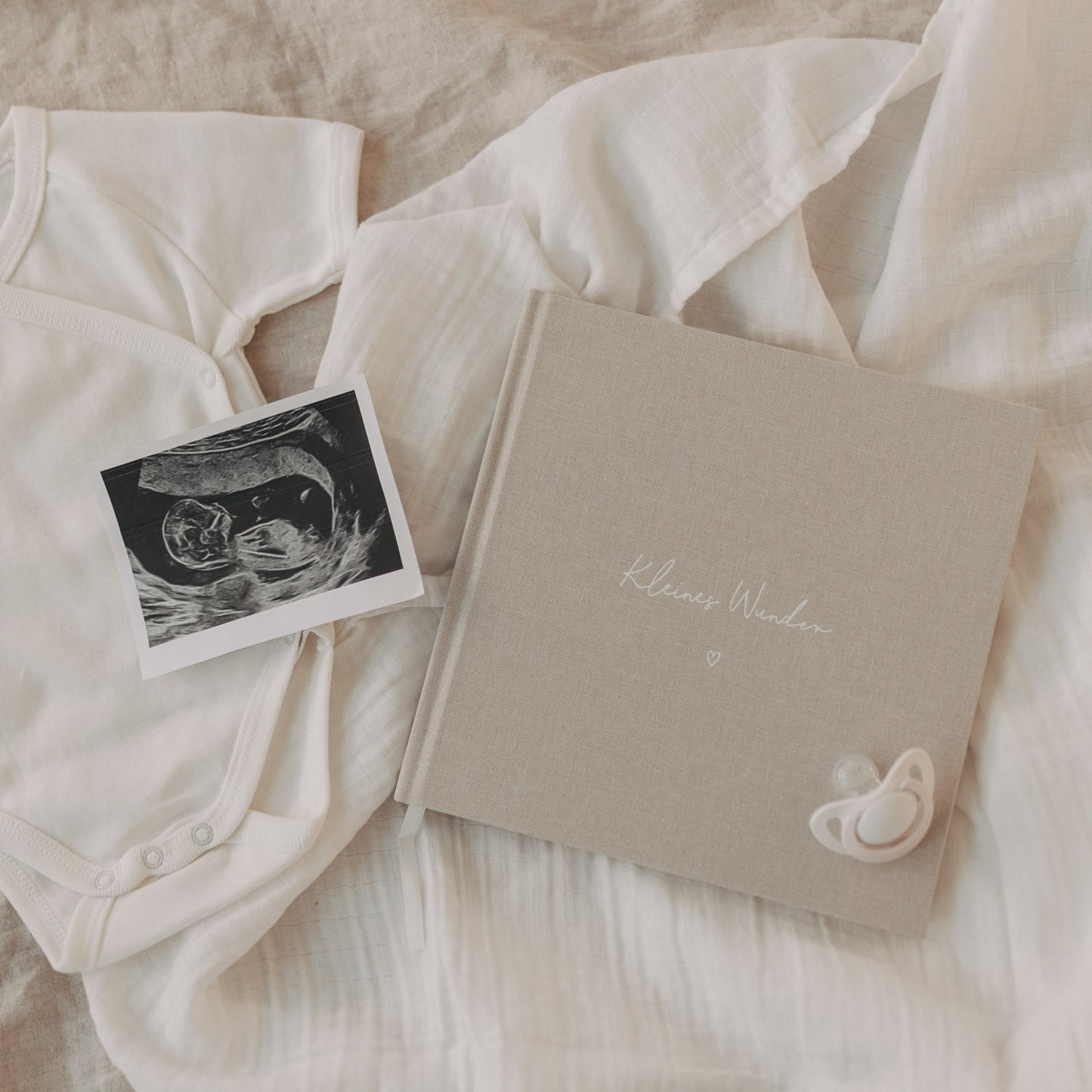 Schwangerschaftstagebuch „Kleines Wunder“ mit Ultraschallbild und Babybody auf weichen Textilien.