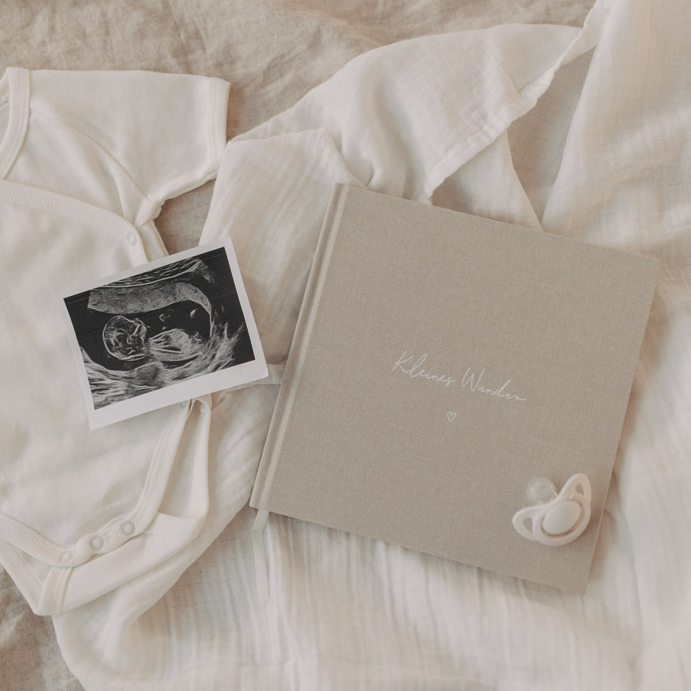 Schwangerschaftstagebuch „Kleines Wunder“ mit Ultraschallbild und Babybody auf weichen Textilien.